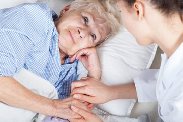 ältere Dame liegt im Bett, Krankenschwester hält ihr die Hand