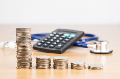 STACKED US QUARTER COINS WITH BLUR BLACK CALCULATOR AND BLUE STETHOSCOPE IN BACKGROUND (MEDICATION CONCEPT)